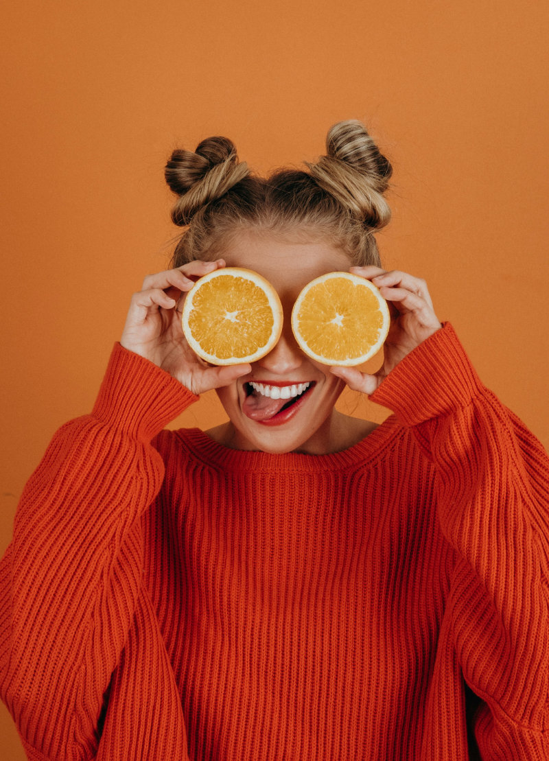 Smiling woman holding orange halves over her eyes playfully.